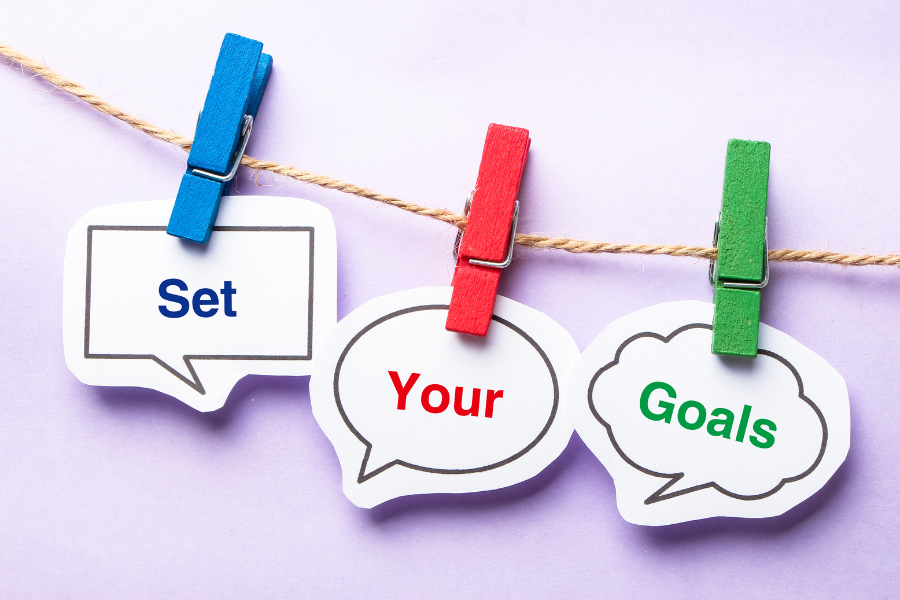 Set your goals paper bubblies with clip handing on the line against purple background.